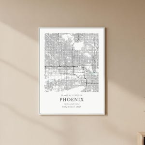 May include: Framed black and white map print of Phoenix, Arizona. The print includes the city's coordinates, the city name, and the text "Home sweet home" with a couple's names and a year.