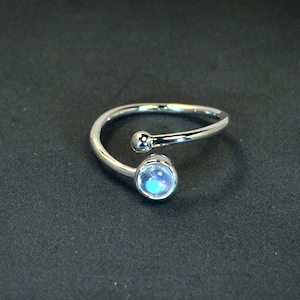 Peut inclure: Une bague en argent avec une pierre de lune ronde et irisée et une petite boule d'argent sur la bande.