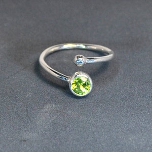 May include: A silver ring with a green gemstone. The ring is designed with a single band that wraps around the finger and a small ball on the opposite side of the gemstone.