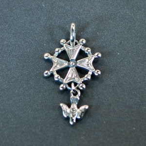 Peut inclure: Pendentif en argent avec une croix et un charme de colombe suspendu en bas. La croix est entourée d'un cercle de petites perles.