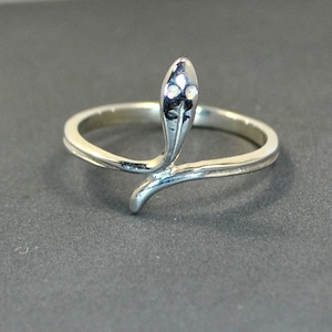 Peut inclure: Une bague en argent en forme de serpent avec une tête de serpent surélevée et trois petites pierres sur la tête. Le serpent est enroulé autour de la bande de la bague.