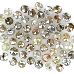 May include: A collection of raw, uncut diamonds in various shades of brown, gray, and yellow. The diamonds are scattered on a white surface, showcasing their unique, irregular shapes and natural textures. The gemstones vary in size and clarity.
