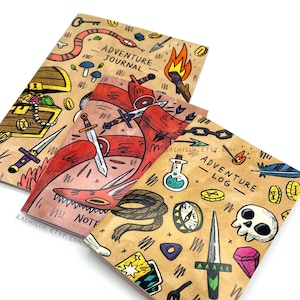 Può includere: Tre piccoli quaderni di carta marrone con illustrazioni colorate. Le copertine presentano uno scrigno del tesoro, un drago rosso e un teschio con una bussola, una pozione e altri elementi fantastici. I quaderni sono intitolati "Adventure Journal" e "Adventure Log".