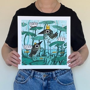May include: Square art print featuring two whimsical birds with crowns, standing in a pond with lily pads and fish. The illustration has a light blue background with rain and white water lilies. The birds have large, round eyes.