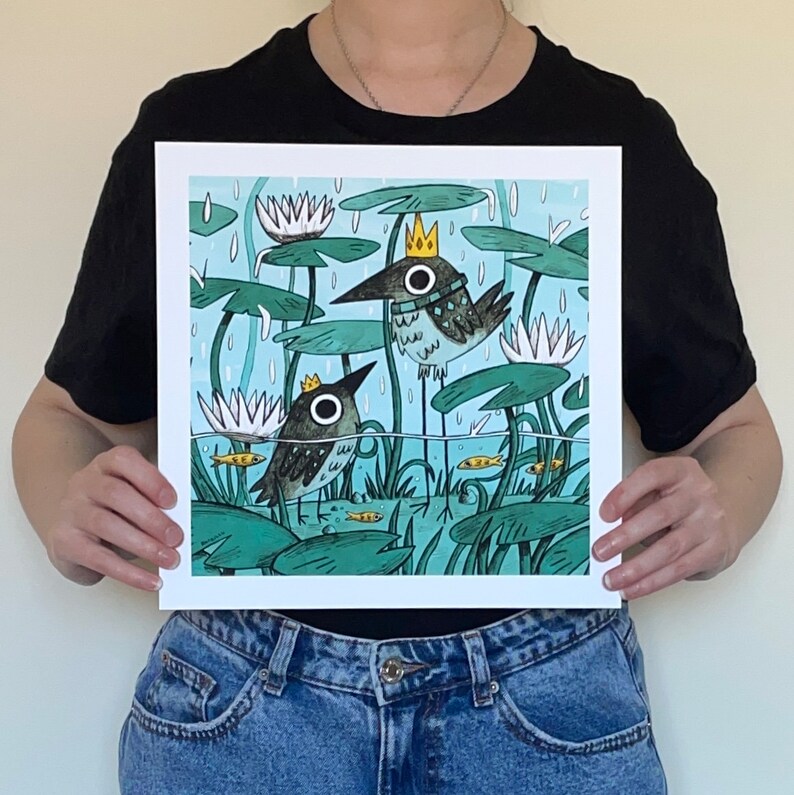 May include: Square art print featuring two whimsical birds with crowns, standing in a pond with lily pads and fish. The illustration has a light blue background with rain and white water lilies. The birds have large, round eyes.