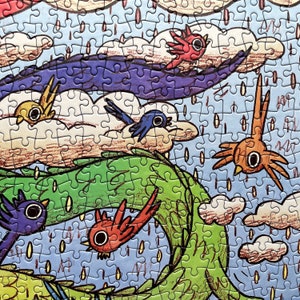 May include: A jigsaw puzzle featuring a colorful illustration of stylized birds flying through a sky filled with white clouds, a large purple wave, and a green winding shape, all set against a light blue background with falling rain drops.