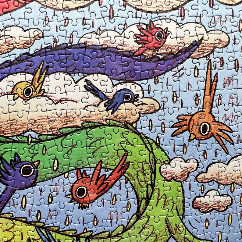 May include: A jigsaw puzzle featuring a colorful illustration of stylized birds flying through a sky filled with white clouds, a large purple wave, and a green winding shape, all set against a light blue background with falling rain drops.