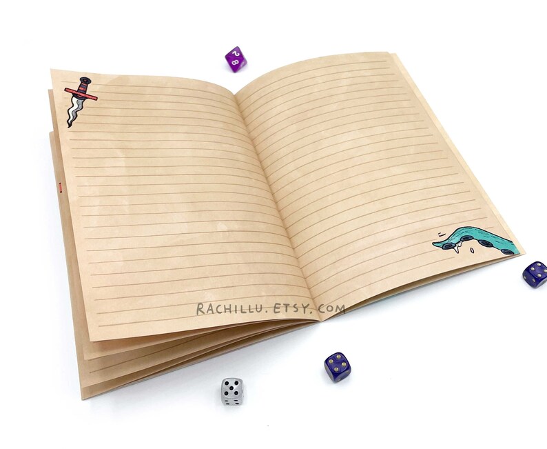 May include: Open brown notebook with lined pages, featuring a red and black dagger illustration on the left page and a green and blue sea serpent illustration on the right page.  The notebook is surrounded by blue dice.