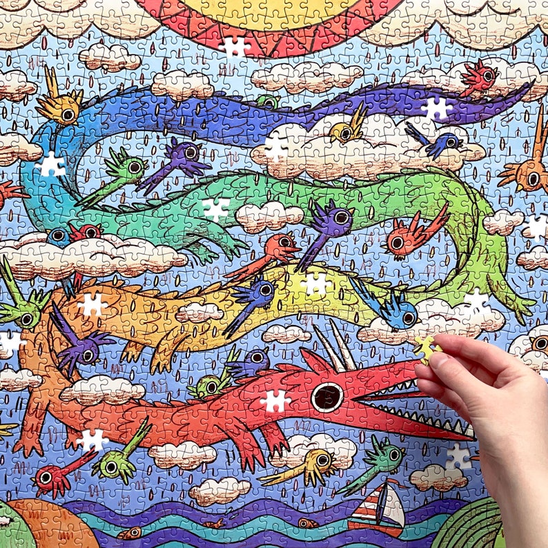 May include: A jigsaw puzzle featuring a colorful illustration of multiple long, serpentine dragons in shades of blue, green, orange, and red flying through a sky filled with clouds, rain, and small birds, with a hand placing a final piece.