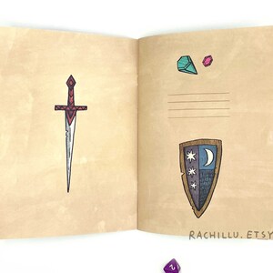 May include: An open notebook with a brown cover. The left page has a drawing of a red and silver sword. The right page has a drawing of a shield with a crescent moon and stars, and two small drawings of gemstones. The text "RACHILLU.ETSY.COM" is printed at the bottom of the right page.