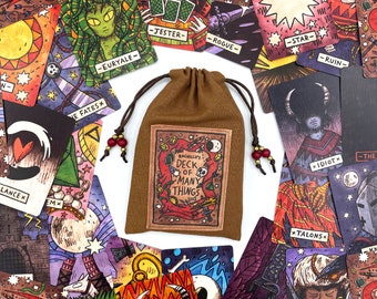 May include: A brown cloth bag with a drawstring closure, containing a deck of cards. The bag has a label that reads "Racailly's Deck of Many Things". The cards are illustrated with various characters and symbols, including a star, a jester, a rogue, and a creature with horns.