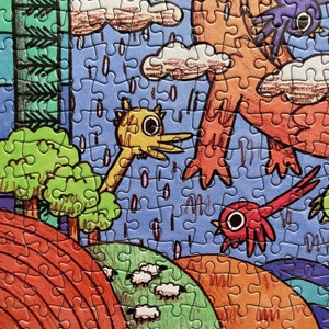 May include: A jigsaw puzzle featuring a colorful illustration of a yellow bird-like creature, a red bird, and a large orange figure under a rainy blue sky. The scene includes green trees, rolling hills, and small white sheep on a landscape.