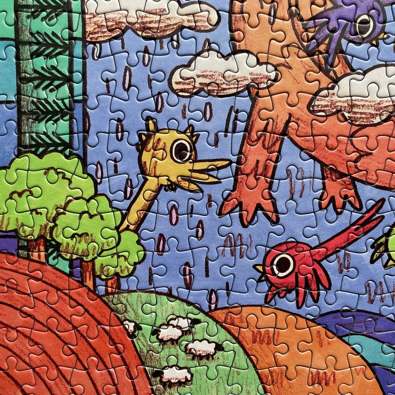 May include: A jigsaw puzzle featuring a colorful illustration of a yellow bird-like creature, a red bird, and a large orange figure under a rainy blue sky. The scene includes green trees, rolling hills, and small white sheep on a landscape.