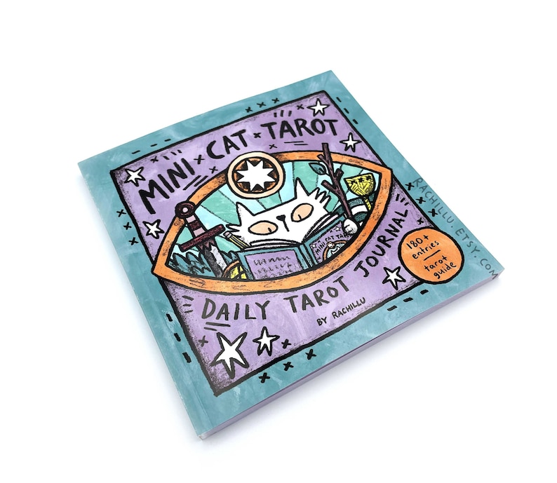 May include: A purple and blue journal with a cat illustration and the text "Mini Cat Tarot Daily Tarot Journal by Rachillu". The journal has a yellow star and the text "180+ entries tarot guide" on the cover.