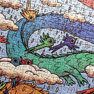 May include: A jigsaw puzzle featuring a colorful illustration of stylized birds in flight against a blue sky with clouds and rain. The scene includes a large green creature, a yellow bird, a green bird, a purple bird, and a blue and red bird.