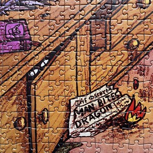 May include: A completed jigsaw puzzle featuring a cartoon illustration. The puzzle depicts a scene with a wooden structure, a purple element, and a sign that reads "The Scayer Man Bites Dragon". A small flame is also visible.