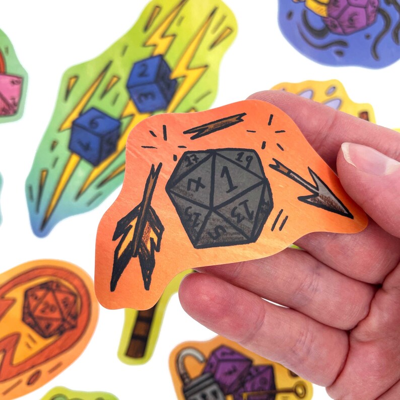 May include: A collection of colorful, hand-drawn stickers featuring dice and fantasy-themed illustrations. One sticker shows a gray twenty-sided die with the number 1, an arrow, and an orange and yellow background.