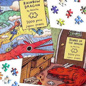 May include: Two 1000 piece jigsaw puzzles by Rachillu titled Rainbow Dragon and Beware of the Dragon. The boxes feature colorful illustrations of red dragons and blue birds, with scattered puzzle pieces visible on a white surface.
