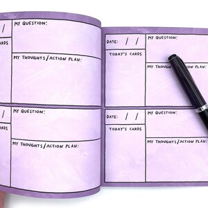 May include: A purple journal with a grid layout for writing down questions, thoughts, and action plans. The journal has the words "Date", "Today's Cards", "My Question", and "My Thoughts/Action Plan" printed on the pages. A black pen is lying on the open journal.