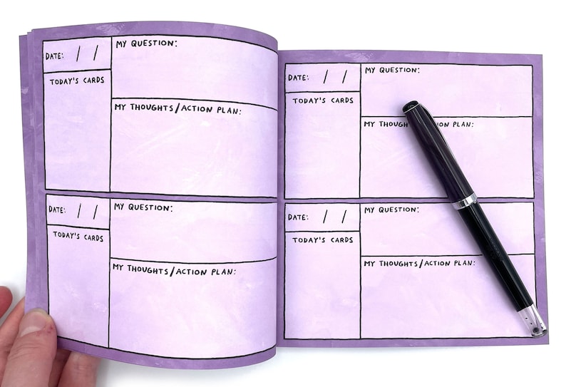 May include: A purple journal with a grid layout for writing down questions, thoughts, and action plans. The journal has the words "Date", "Today's Cards", "My Question", and "My Thoughts/Action Plan" printed on the pages. A black pen is lying on the open journal.