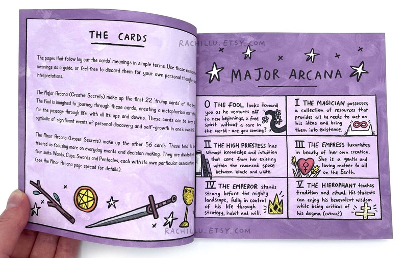 May include: An open book with purple pages and illustrations of tarot cards. The book features the Major Arcana cards, including The Fool, The High Priestess, The Magician, The Empress, and The Hierophant. The text on the page reads "The Cards" and "Major Arcana".