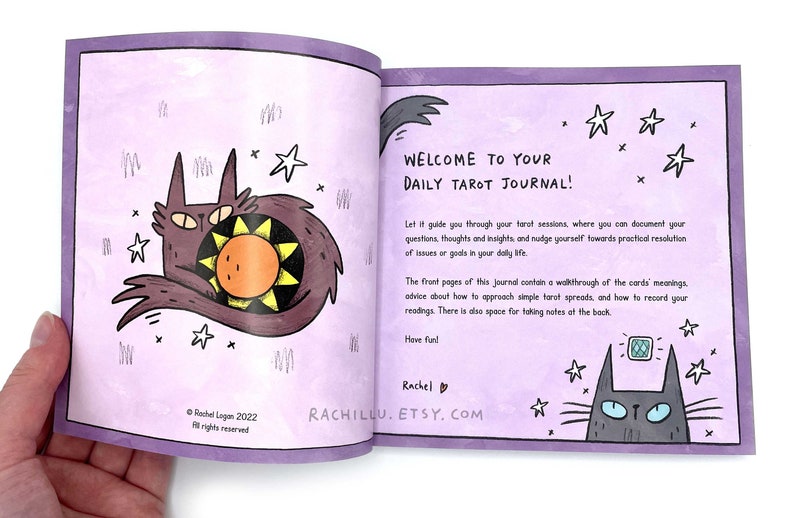 May include: A purple daily tarot journal with a cat and sun illustration on the front cover. The text on the cover reads "Welcome to Your Daily Tarot Journal!" and includes the website "rachillu.etsy.com".