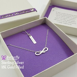 Könnte beinhalten: Eine silberne Unendlichkeitskette mit einem kleinen Anhänger, auf dem "Gosia" in Kursivschrift steht. Die Kette befindet sich in einer weißen Schachtel mit violetter Auskleidung. Die Schachtel hat ein Schmetterlingslogo und den Text "Butterfly zana design Sterling Silver 18K Gold Filled".