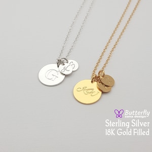 Peut inclure: Deux colliers personnalisés avec des pendentifs initiaux. L'un est argenté avec un grand disque gravé de la lettre "G" et deux petits disques avec les lettres "K" et "S". L'autre est doré avec les initiales "KW" et "R".