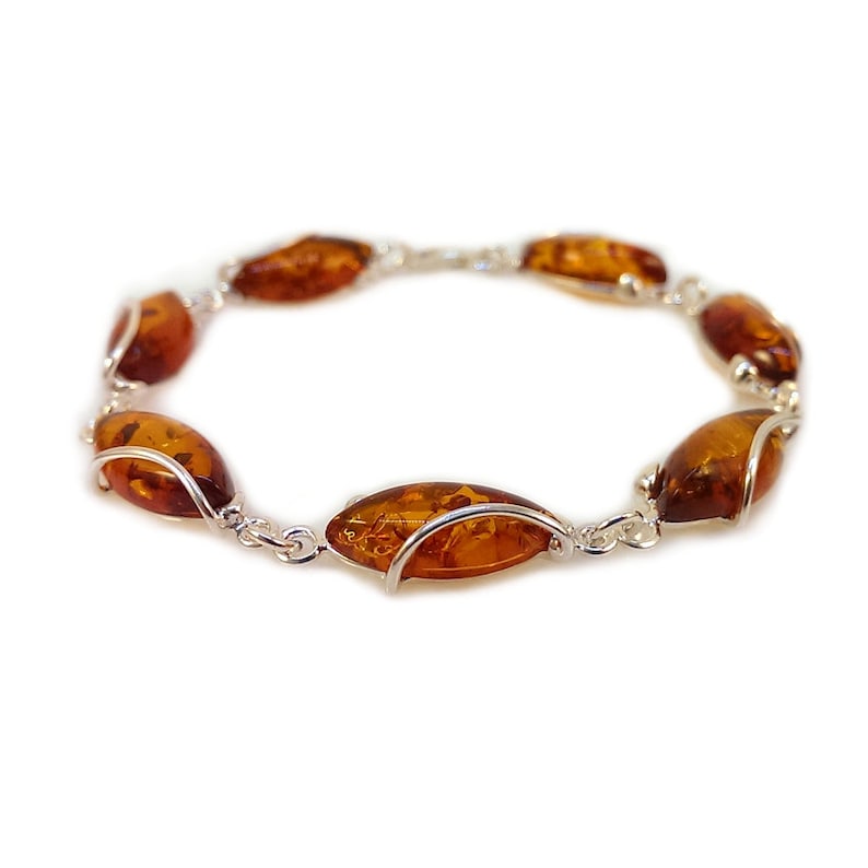 May include: A silver bracelet featuring amber stones. The stones are oval in shape and have a warm, honey colour. The bracelet is made from a delicate chain and has a simple, elegant design.