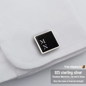 May include: A pair of cufflinks with a black onyx stone set in sterling silver. The stone is engraved with the initials "MN".