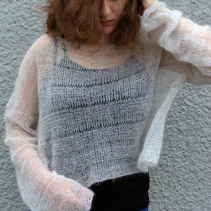 May include: A white, sheer, knitted jumper with long sleeves. The jumper is loose fitting and has a cropped length.
