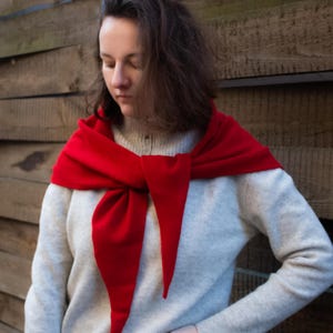 May include: A woman wearing a white sweater with a red scarf tied around her neck. The scarf is tied in a loose knot and the ends are hanging down.