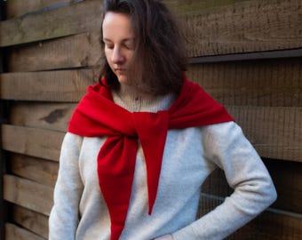 May include: A woman wearing a white sweater with a red scarf tied around her neck. The scarf is tied in a loose knot and the ends are hanging down.