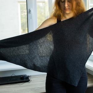 Peut inclure: Une personne tenant une écharpe triangulaire gris foncé en tissu doux et texturé.