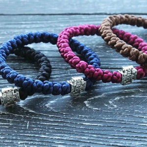 May include: Four braided bracelets with silver charms. The bracelets are in shades of brown, pink, blue, and black.