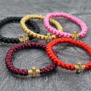 May include: Five colourful knotted bracelets with gold cross charms. The bracelets are in black, gold, pink, red, and burgundy.