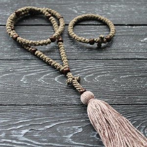 May include: A set of two brown and beige knotted prayer ropes with wooden beads and a tassel. The larger rope has a wooden cross at the end. The smaller rope is a bracelet.