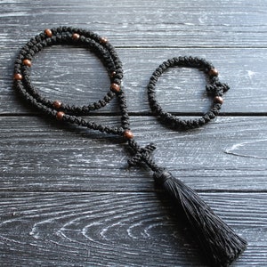 May include: Black prayer beads with brown wooden beads and a black tassel. The beads are strung on a black cord and the tassel is attached to a small black cross.