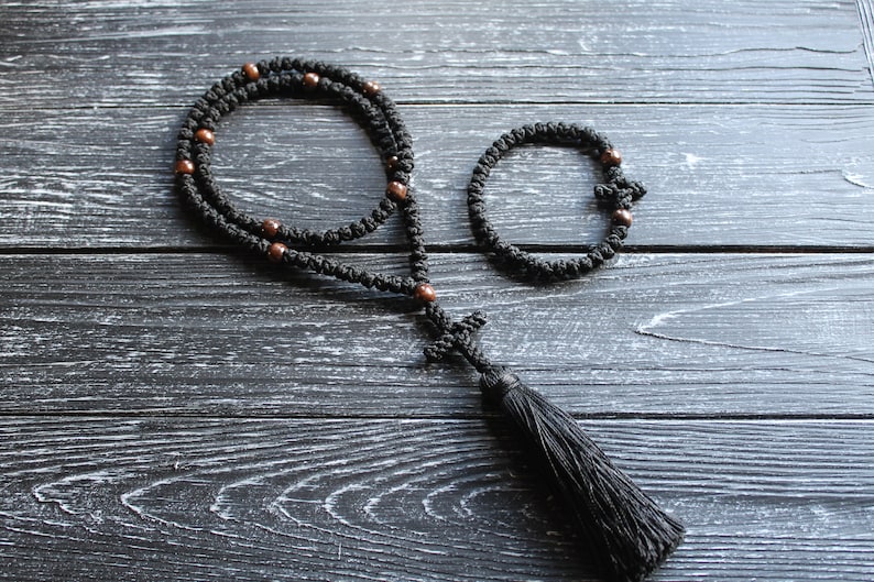 May include: Black prayer beads with brown wooden beads and a black tassel. The beads are strung on a black cord and the tassel is attached to a small black cross.