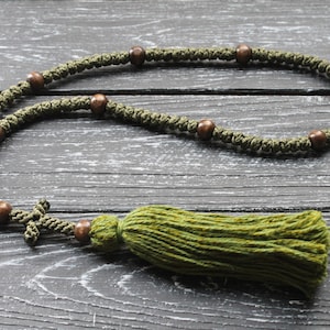 May include: A green prayer rope with brown wooden beads and a green tassel. The rope is laid out on a dark wood surface.