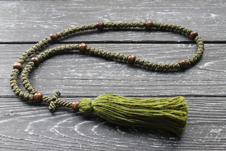 May include: A green prayer rope with brown wooden beads and a green tassel. The rope is laid out on a dark wood surface.