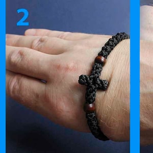 May include: A black braided bracelet with a wooden cross charm and brown wooden beads. The bracelet is worn on a person's wrist.
