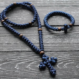 K&ouml;nnte beinhalten: Ein Satz blauer Gebetsperlen mit Holzperlen und einem gekn&uuml;pften Kreuz. Die Perlen sind auf einer Schnur aufgef&auml;delt und das Kreuz befindet sich am Ende der Schnur.