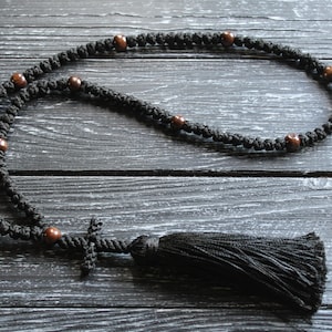 May include: Black prayer beads with brown wooden beads and a black tassel. The beads are strung on a black cord and the tassel is attached to a small black cross.