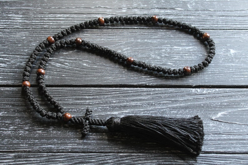 May include: Black prayer beads with brown wooden beads and a black tassel. The beads are strung on a black cord and the tassel is attached to a small black cross.
