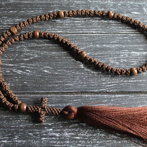 May include: A brown knotted prayer rope with wooden beads and a brown tassel. The rope has a small brown cross at the end.