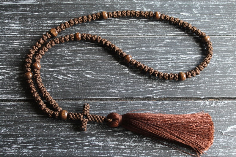 May include: A brown knotted prayer rope with wooden beads and a brown tassel. The rope has a small brown cross at the end.