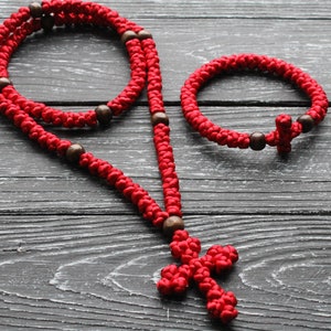 K&ouml;nnte beinhalten: Rotes Gebetsseil mit Holzperlen und einem Kreuzanh&auml;nger. Das Seil ist gekn&uuml;pft und hat ein kleineres rotes Armband mit einem Kreuzanh&auml;nger.