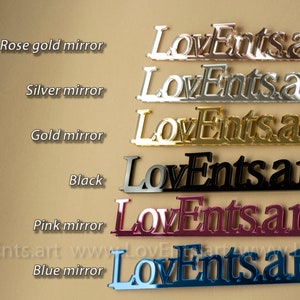 K&ouml;nnte beinhalten: Eine Pr&auml;sentation von "LoveEnts.art"-Schildern in verschiedenen Farben: Ros&eacute;gold, Silber, Gold, Schwarz, Pink Mirror und Blau Mirror. Die Schilder bestehen aus einem reflektierenden Material, mit dem Text in einer stilisierten Schriftart. Die Website-Adresse ist unten sichtbar.