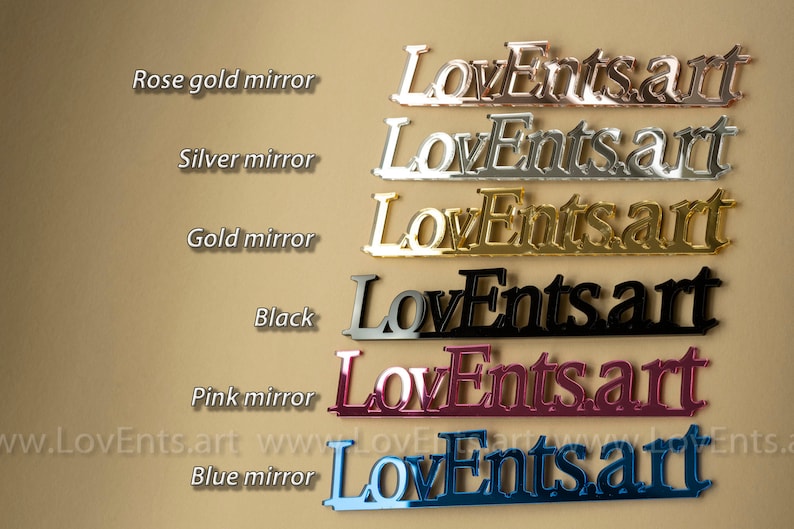 K&ouml;nnte beinhalten: Eine Pr&auml;sentation von "LoveEnts.art"-Schildern in verschiedenen Farben: Ros&eacute;gold, Silber, Gold, Schwarz, Pink Mirror und Blau Mirror. Die Schilder bestehen aus einem reflektierenden Material, mit dem Text in einer stilisierten Schriftart. Die Website-Adresse ist unten sichtbar.